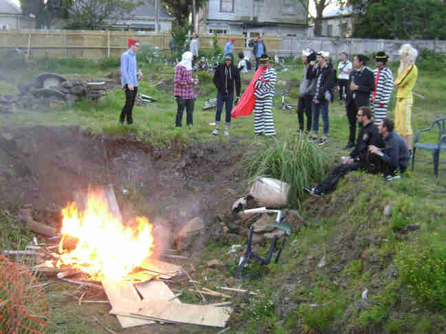 People wearing costumes, standing in a grass field, above a pit with a bonfire in it